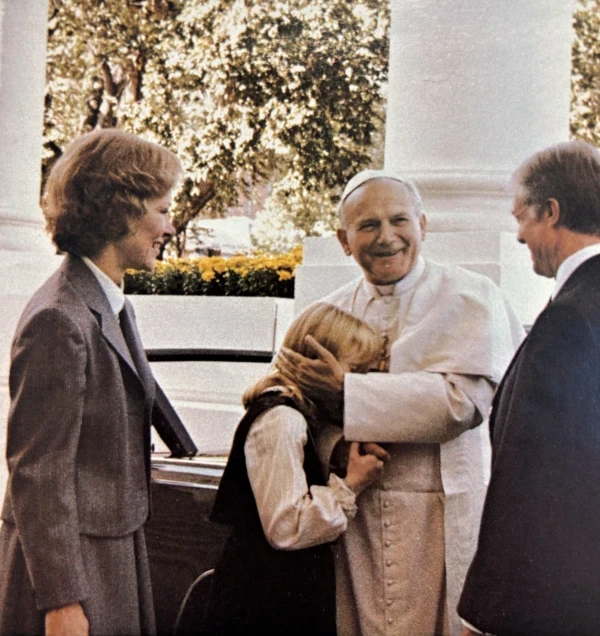 Ante la mirada radiante del presidente estadounidense Jimmy Carter y de la primera dama Rosalynn Carter, el Papa San Juan Pablo II saluda a la hija de ambos Amy Carter, que entonces tenía 11 años, a su llegada a la Casa Blanca el 6 de octubre de 1979. Crédito: Oficina de Imprenta del Gobierno de EE. UU.
